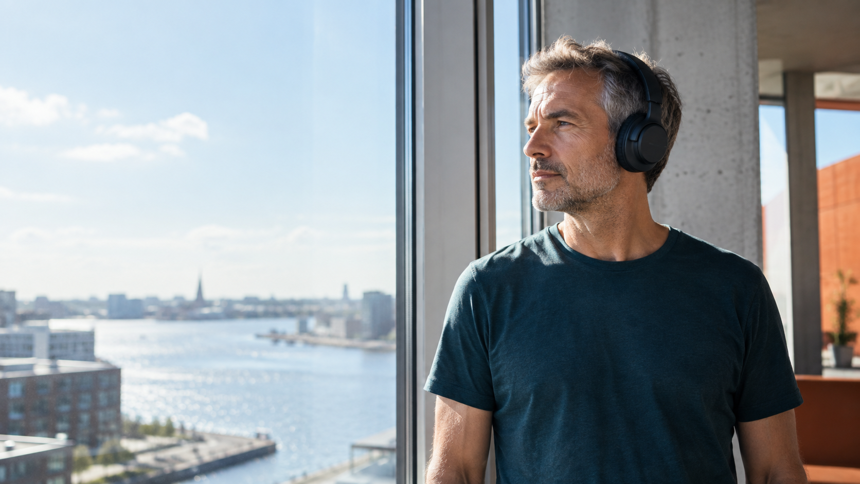 Mand med hovedtelefoner ved et stort vindue i dagslys.